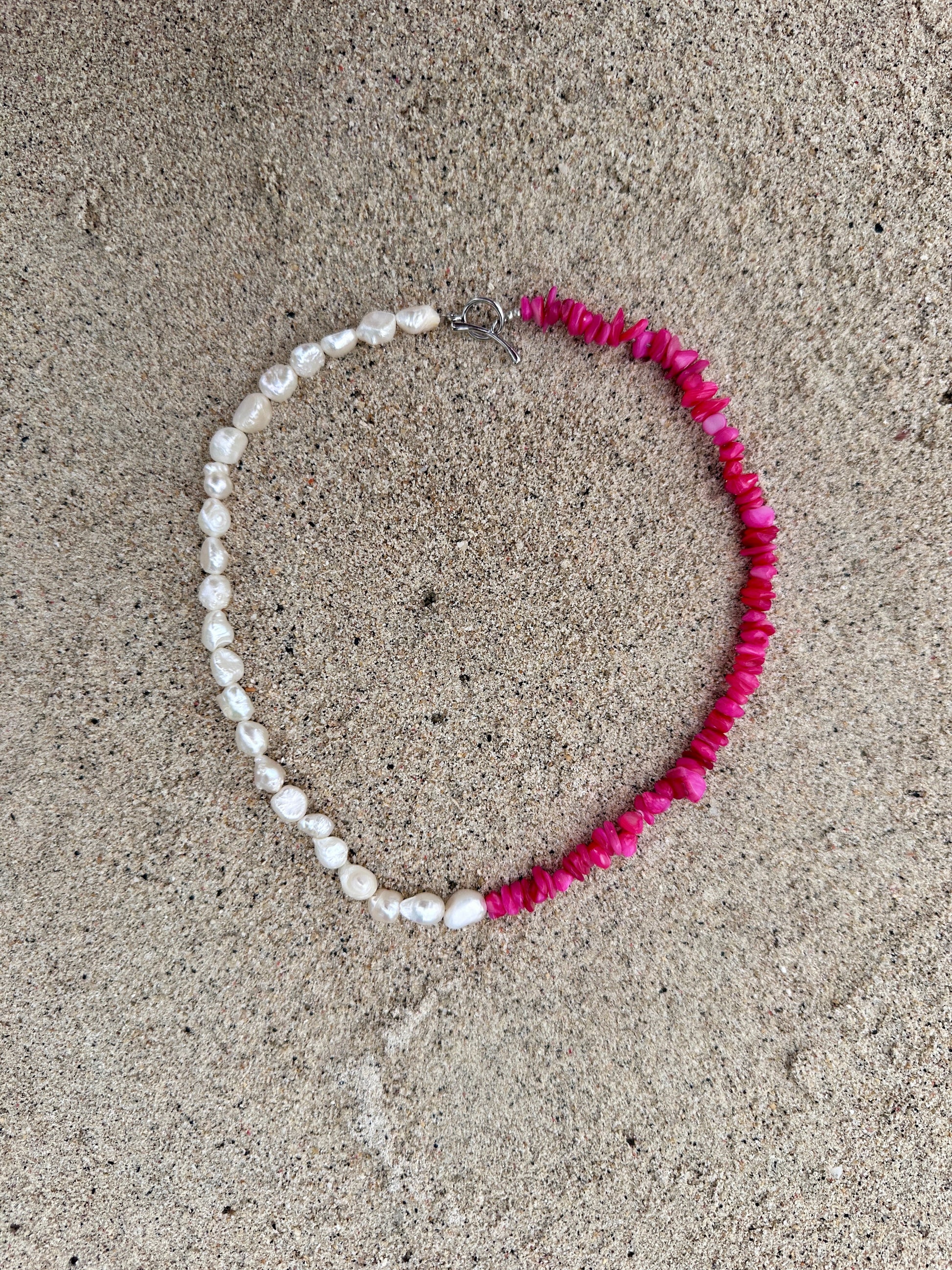 Necklace with corals and freshwater pearls on a sandy surface