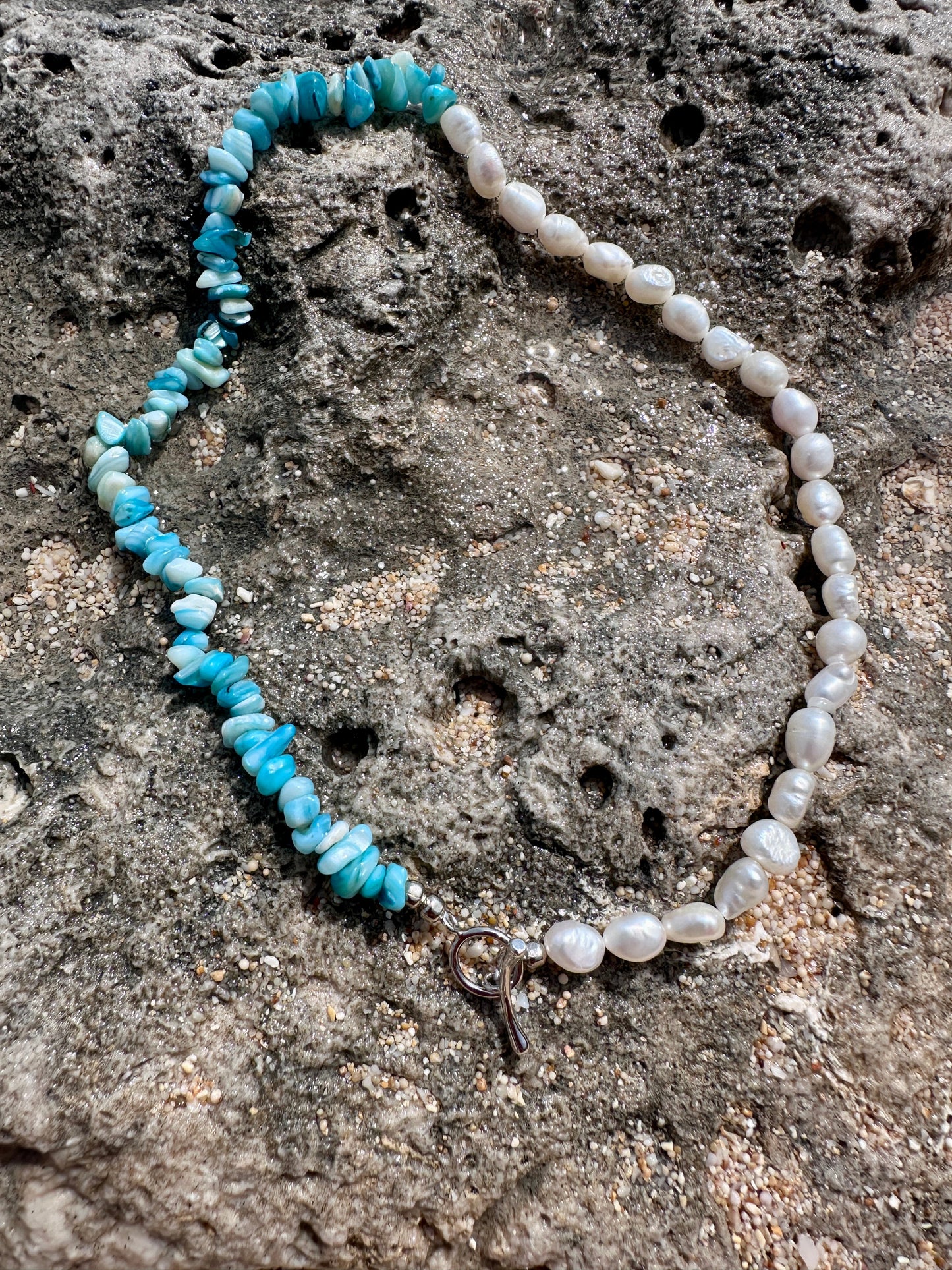 Necklace with blue stones and freshwater pearls on a textured stone surface